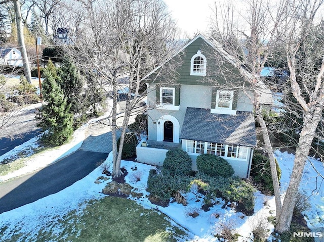 view of front facade with stucco siding, driveway, and roof with shingles