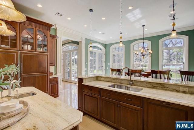 kitchen with light stone counters, sink, crown molding, and hanging light fixtures