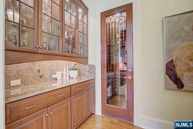 bar featuring tasteful backsplash, light stone countertops, and light hardwood / wood-style floors