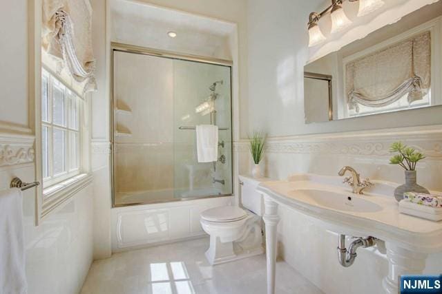 full bathroom featuring toilet, shower / bath combination with glass door, tile patterned flooring, and sink