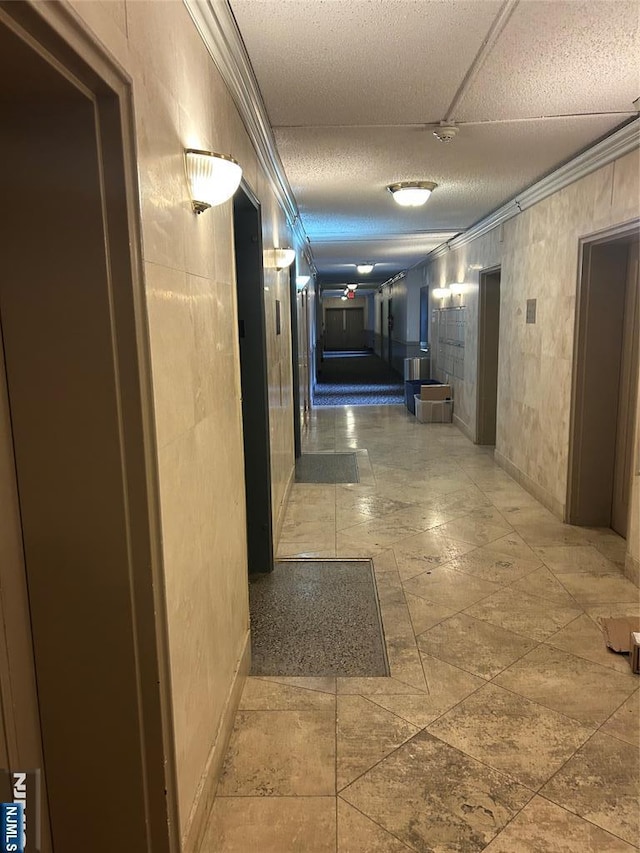 hallway with a textured ceiling, baseboards, and ornamental molding