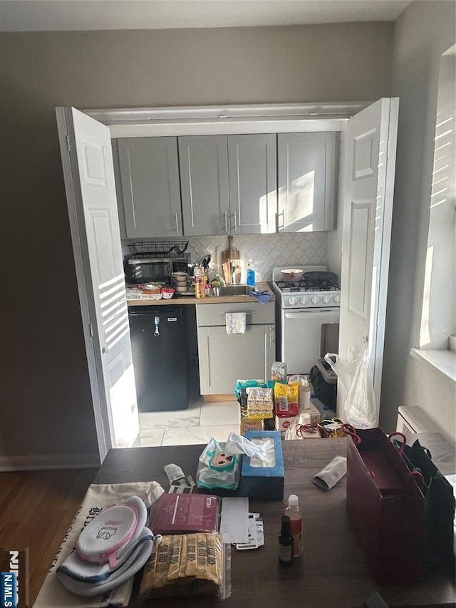 kitchen with decorative backsplash, dishwashing machine, gray cabinets, and white gas range oven