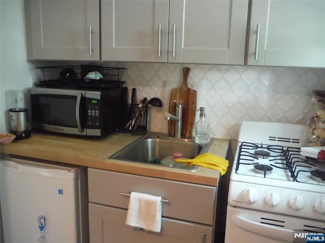 kitchen with white range with gas cooktop, a sink, stainless steel microwave, decorative backsplash, and dishwasher