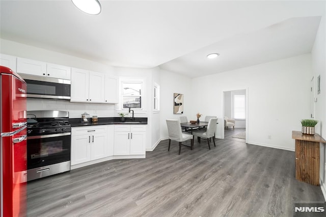 kitchen with sink, white cabinetry, stainless steel appliances, wood-type flooring, and decorative backsplash