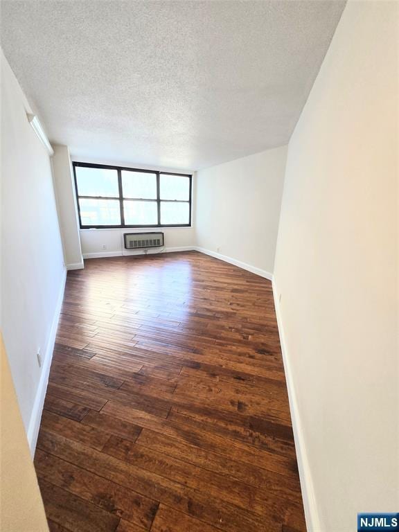 unfurnished room with a wall unit AC, dark hardwood / wood-style floors, and a textured ceiling