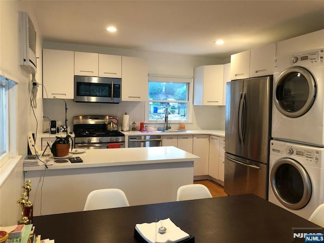 kitchen featuring appliances with stainless steel finishes, a wall mounted air conditioner, stacked washer / dryer, sink, and white cabinets