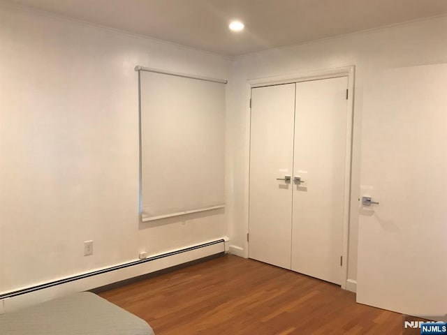 unfurnished bedroom featuring hardwood / wood-style flooring, ornamental molding, baseboard heating, and a closet