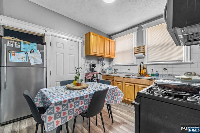 kitchen with light hardwood / wood-style flooring, stainless steel refrigerator, black range with gas cooktop, light stone counters, and decorative backsplash