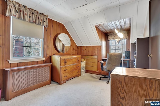 carpeted office space featuring vaulted ceiling, radiator, and wooden walls