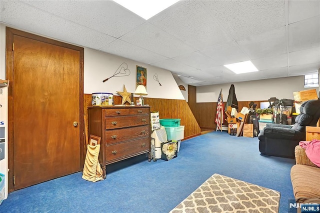 recreation room with carpet, a drop ceiling, and wood walls