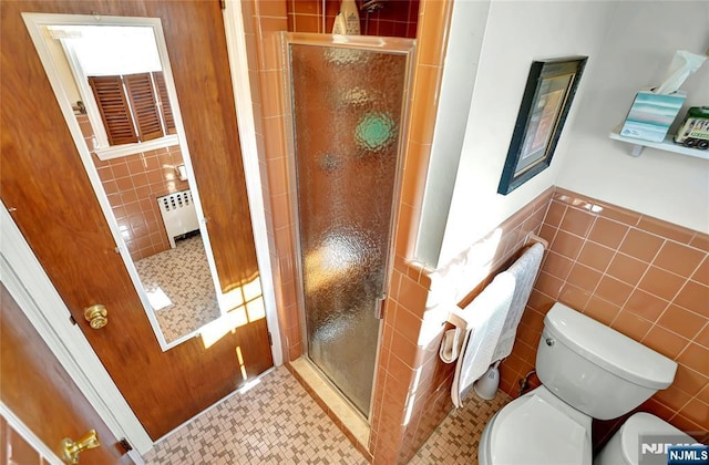 bathroom featuring a shower with door, tile walls, radiator heating unit, tile patterned floors, and toilet