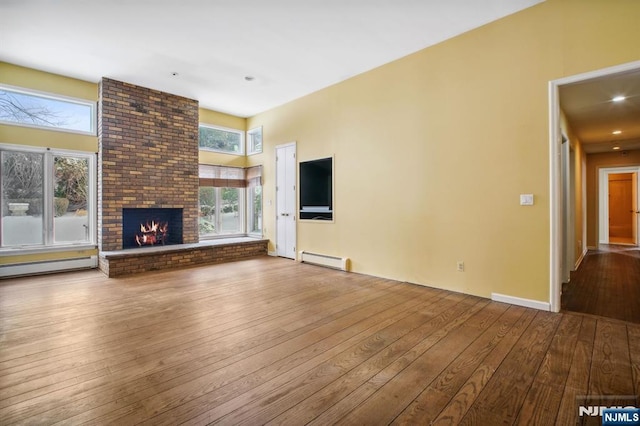 unfurnished living room with a brick fireplace, hardwood / wood-style floors, and baseboard heating