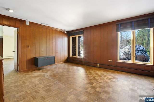 empty room featuring crown molding, a baseboard radiator, wooden walls, and light parquet floors