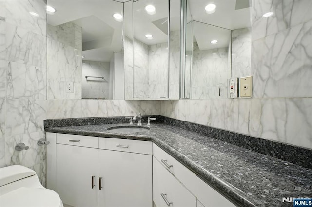 bathroom with vanity, toilet, and tile walls