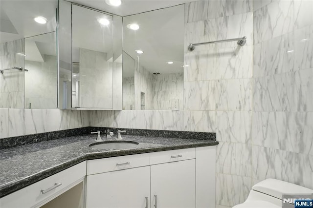 bathroom featuring walk in shower, vanity, toilet, and tile walls