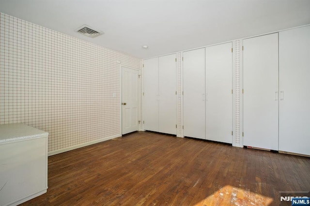 unfurnished bedroom featuring dark wood-type flooring and multiple closets