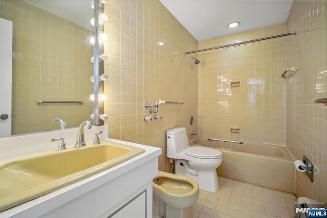 full bathroom featuring a bidet, tile walls, vanity, toilet, and tiled shower / bath