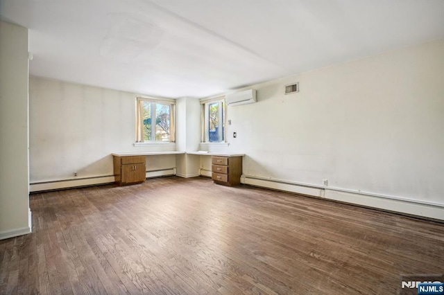 unfurnished room featuring dark wood-type flooring, built in desk, a wall unit AC, and a baseboard radiator