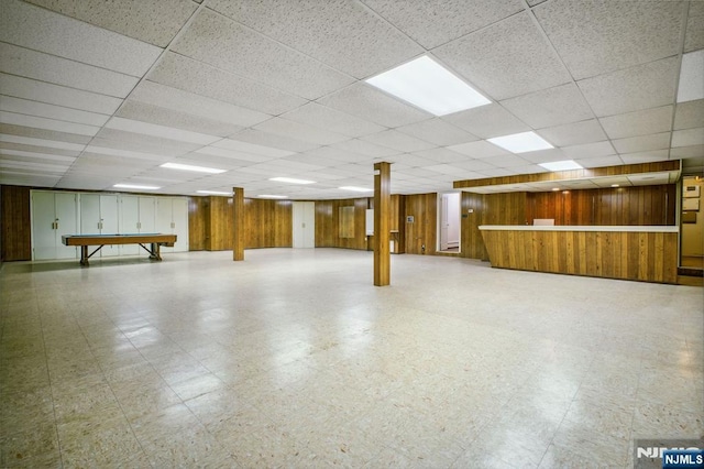 basement featuring wooden walls and a drop ceiling