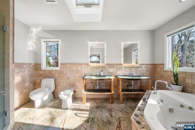 bathroom featuring a bidet, toilet, a bathing tub, and tile walls