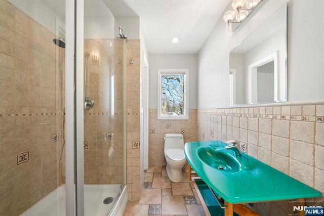 bathroom featuring toilet, a shower with shower door, and tile walls