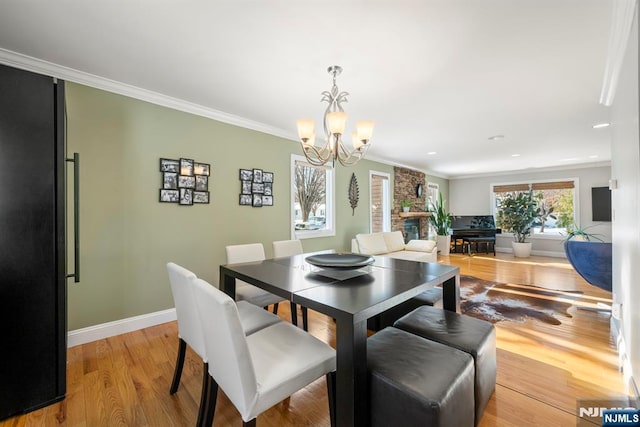 dining area with an inviting chandelier, crown molding, a fireplace, and light wood-type flooring