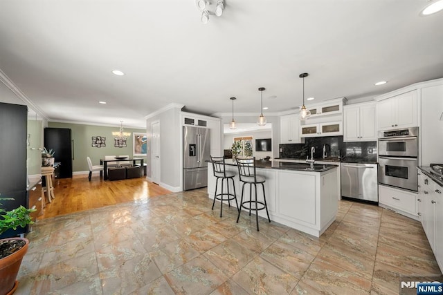 kitchen with appliances with stainless steel finishes, decorative light fixtures, tasteful backsplash, white cabinetry, and a kitchen bar