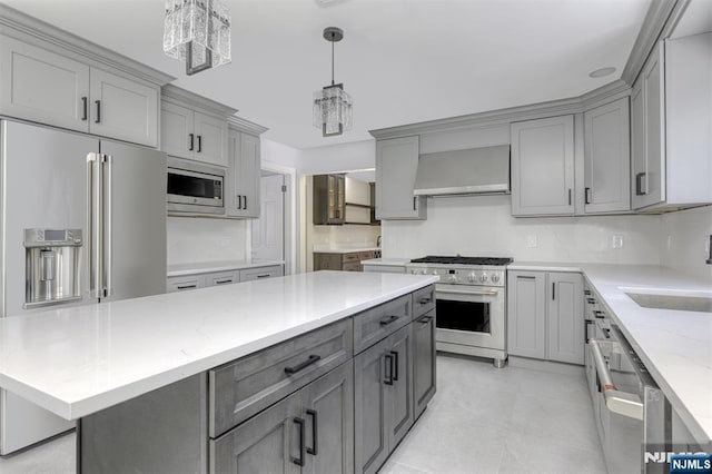 kitchen with wall chimney exhaust hood, gray cabinetry, high end appliances, a chandelier, and hanging light fixtures