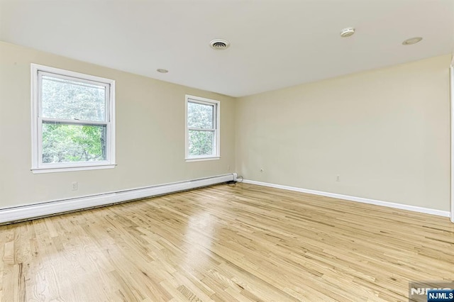 unfurnished room featuring a baseboard heating unit, light hardwood / wood-style floors, and a healthy amount of sunlight