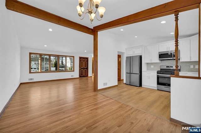 kitchen featuring appliances with stainless steel finishes, pendant lighting, white cabinets, decorative backsplash, and light hardwood / wood-style floors