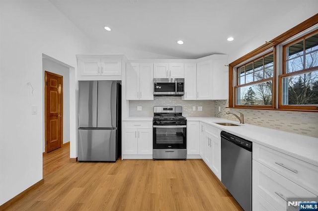 kitchen featuring vaulted ceiling, appliances with stainless steel finishes, white cabinetry, sink, and light wood-type flooring