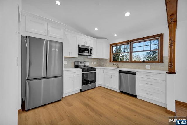 kitchen with tasteful backsplash, white cabinetry, sink, stainless steel appliances, and light wood-type flooring