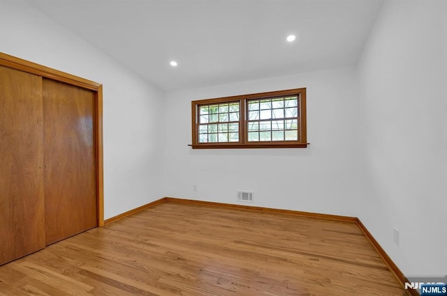 unfurnished bedroom featuring lofted ceiling, a closet, and light wood-type flooring