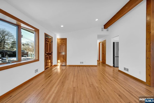 spare room featuring lofted ceiling with beams and light hardwood / wood-style floors