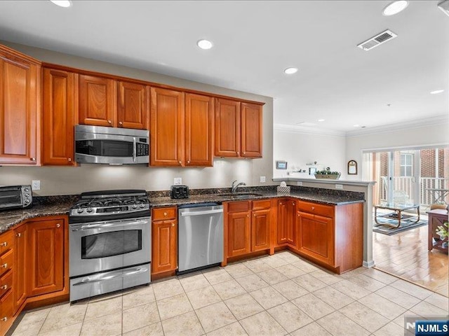 kitchen with sink, ornamental molding, appliances with stainless steel finishes, kitchen peninsula, and dark stone counters