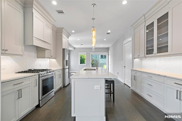 kitchen featuring sink, a breakfast bar area, appliances with stainless steel finishes, an island with sink, and decorative light fixtures