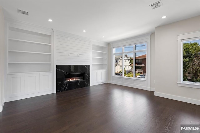 unfurnished living room featuring a high end fireplace, dark hardwood / wood-style floors, and built in features