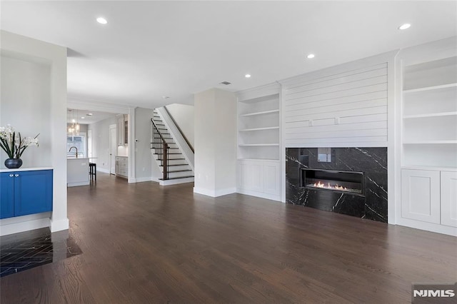 unfurnished living room with built in shelves, dark wood-type flooring, and a premium fireplace