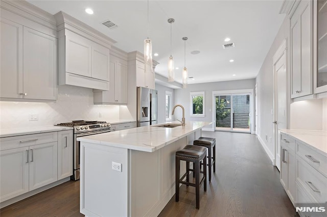 kitchen featuring an island with sink, white cabinetry, sink, hanging light fixtures, and stainless steel appliances