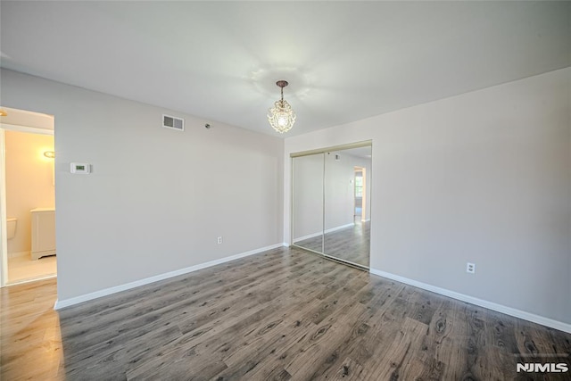 unfurnished bedroom featuring hardwood / wood-style floors, a closet, and a chandelier