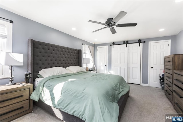 bedroom with ceiling fan, light colored carpet, a barn door, and multiple closets