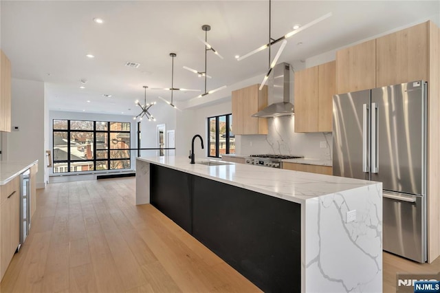 kitchen featuring a large island with sink, light stone countertops, stainless steel fridge, and wall chimney exhaust hood