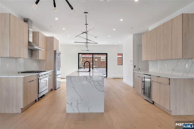 kitchen with wine cooler, light brown cabinetry, high end appliances, a kitchen island with sink, and wall chimney range hood