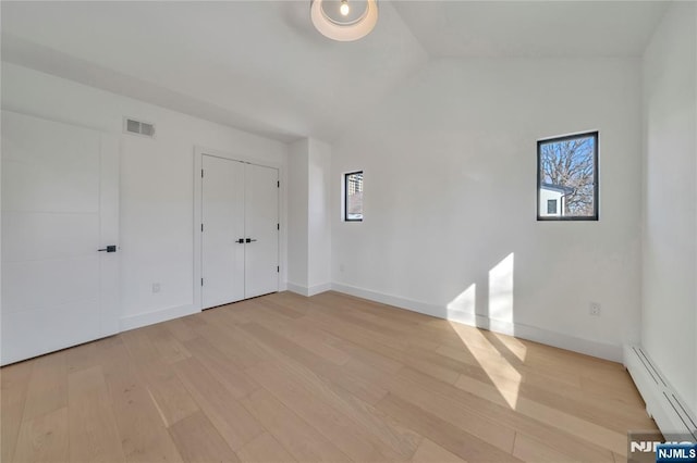 empty room featuring a baseboard radiator, vaulted ceiling, a wealth of natural light, and light hardwood / wood-style flooring