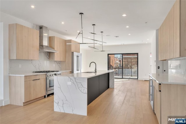 kitchen featuring wall chimney exhaust hood, sink, premium appliances, pendant lighting, and a kitchen island with sink