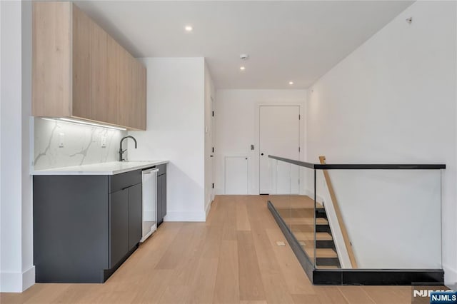 kitchen with tasteful backsplash, dishwasher, sink, light stone counters, and light hardwood / wood-style flooring