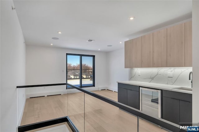 kitchen featuring sink, beverage cooler, backsplash, light brown cabinets, and light wood-type flooring