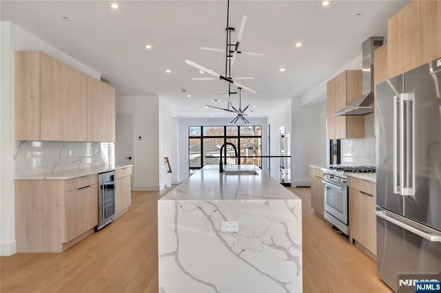 kitchen featuring wall chimney exhaust hood, sink, a center island with sink, premium appliances, and beverage cooler