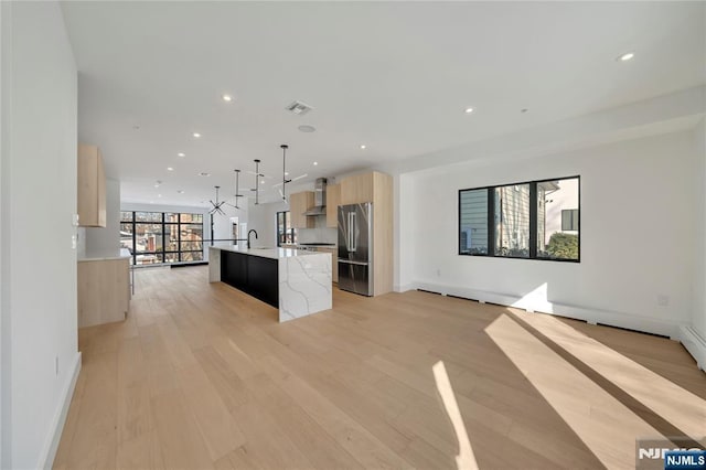 kitchen featuring sink, a center island with sink, light brown cabinets, high quality fridge, and pendant lighting