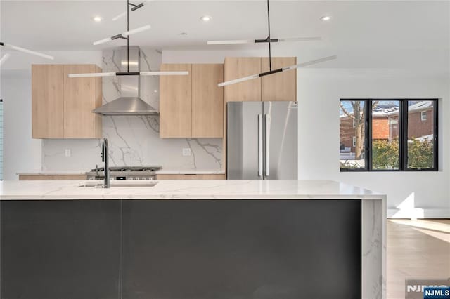 kitchen with appliances with stainless steel finishes, backsplash, light stone counters, light brown cabinets, and light hardwood / wood-style flooring